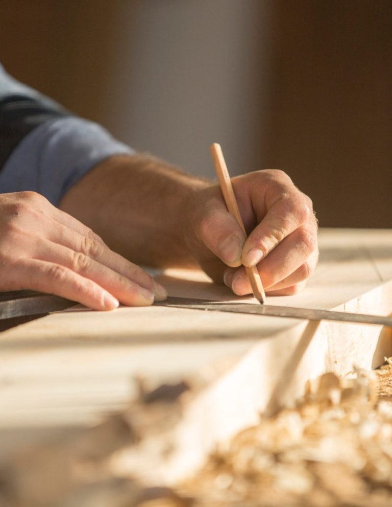 Timmerman met potlood Een hand die met een potlood op een stuk hout tekent.