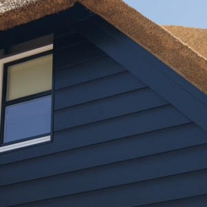 Keralit potdeksel Zwarte houten gevel met een enkel raam en een schuine, rieten dakrand.