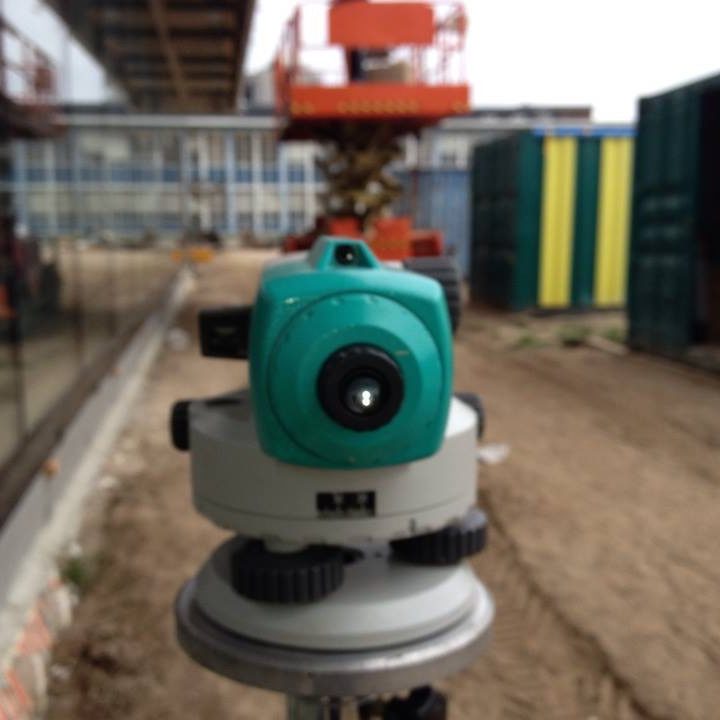 Waterpastoestel Groene theodoliet geplaatst op een bouwlocatie met containers op de achtergrond.